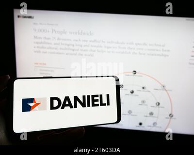 Person, die ein Mobiltelefon mit dem Logo des italienischen Unternehmens Danieli C. Officine Meccaniche Spa vor der Webseite des Unternehmens hält. Schwerpunkt auf dem Display des Telefons. Stockfoto