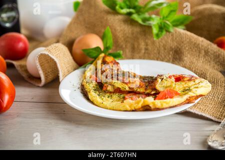 Gefülltes Omelett mit Tomaten auf hellem Holzgrund. Gesunde Ernährung zum Frühstück. Stockfoto