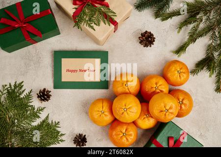 Mandarinen und Grußkarte für das frohe neue Jahr in der Nähe von Geschenkboxen mit saisonalem Dekor auf strukturierter Oberfläche Stockfoto