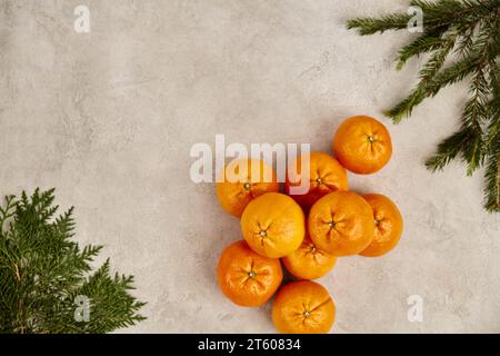 Weihnachtlicher Hintergrund, reife Mandarinen mit wacholder- und Kiefernzweigen auf grauer strukturierter Oberfläche Stockfoto