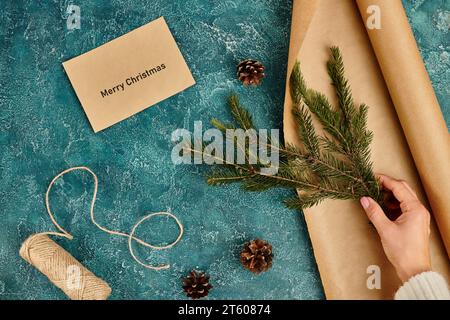 Zugeschnittene Ansicht einer Frau mit Kiefernzweig in der Nähe eines Umschlags mit „Merry Christmas“-Schriftzug und diy-Zubehör Stockfoto