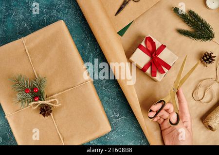 Zugeschnittene Ansicht einer Frau mit Schere in der Nähe von Geschenkboxen Weihnachtsdekorationsmaterialien auf blauer Textur Stockfoto