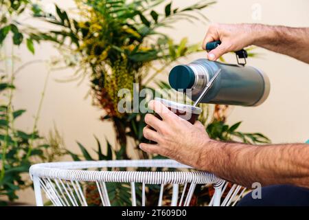 Ein Mann gießt Wasser aus einer Thermoskanne in einen Gefährten im Garten. Stockfoto