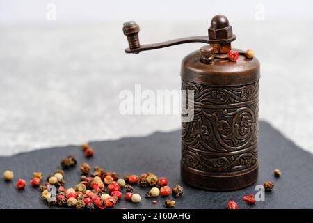 Eine alte Pfeffer- und Gewürzmühle aus Metall auf Schieferfliesen, auf hellem Hintergrund Stockfoto
