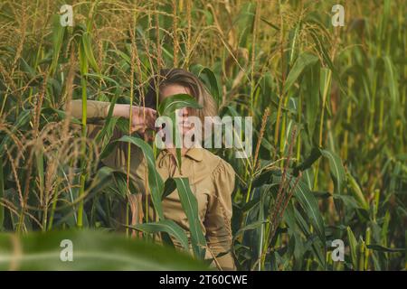 Blondes Mädchen mit schlanker Figur, das sich im Sommer auf dem Maisfeld entspannt. Das schöne, allein stehende Mädchen im Maisgarten genießt einen Moment. Stockfoto