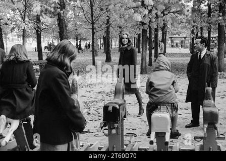 1960er Jahre, Frauen-Models und Mann sehen Kinder auf einem Pferdekarussell spielen, Jardin des Tuileries Garten, Paris, Frankreich, Europa, Stockfoto