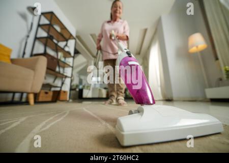 Eine ältere Frau saugt staubigen Teppich in ihrer Wohnung ab Stockfoto