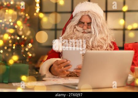 Weihnachtsmann mit Tablet-PC zu Hause am Weihnachtsabend Stockfoto