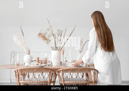 Schöne Frau, die einen Tisch mit getrockneten Blumen im Esszimmer legt Stockfoto