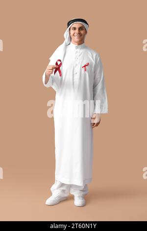Schöner muslimischer Mann mit roten Bändern auf braunem Hintergrund. AID Awareness-Konzept Stockfoto