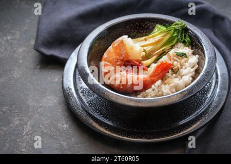 Frittierte Riesengarnelen oder Garnelen mit Reis und pak Choi in einer schwarz gepunkteten Keramikschale auf dunklem Hintergrund, kochen im asiatischen Stil, Kopierraum, ausgewählt Stockfoto