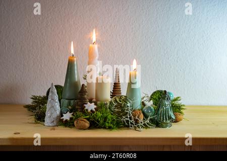 3. Adventszeit, Dekoration mit vier verschiedenen Kerzen, drei sind beleuchtet, einige Moose, grüne Weihnachtskugeln aus Glas und Zimtsterne auf einem Holzbrett Stockfoto