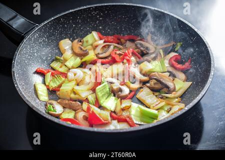 Das dampfende Gemüse wird in einer Pfanne mit gesunden Zutaten wie Paprika, Pilzen, Zwiebeln und Kohl gebraten Stockfoto