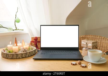 Mockup eines weißen Laptop-Bildschirms auf einem Holzschreibtisch mit Geschenken, Adventskerzen und Weihnachtsdekoration in einer Dachwohnung, Urlaub Online Shopping, c Stockfoto