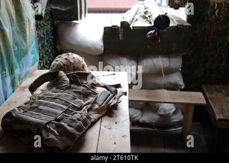 Ein Militärhelm eines ukrainischen Soldaten mit einer schweren kugelsicheren Weste auf einem Holztisch im Innenraum des Kontrollpunktes Stockfoto