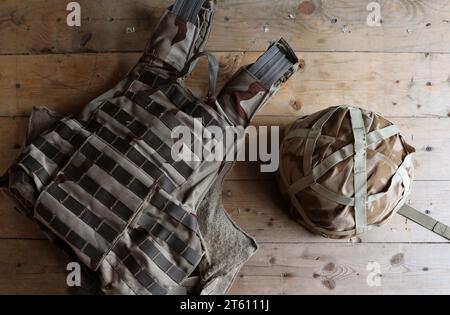 Ein Militärhelm eines ukrainischen Soldaten mit einer schweren kugelsicheren Weste auf einem Holztisch im Innenraum des Kontrollpunktes Stockfoto