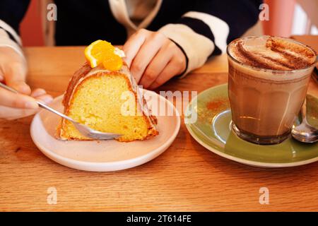 Frau genießt Kürbis Chai, während sie Orangenkuchen in einem Café in Nijmegen, Niederlande isst Stockfoto