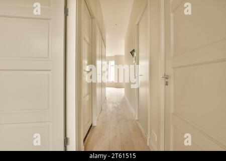 Ein langer Flur mit weißen Wänden und Holzfußboden auf jeder Seite, der zu den anderen Zimmern führt Stockfoto