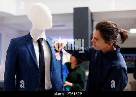 Lächelnder asiatischer Kunde, der während des Black Friday im Bekleidungsgeschäft auf rotem Preisschild blickt. Einzelhandelsmitarbeiter, die visuelles Merchandising herstellen und Modeboutiquen für den Verkauf vorbereiten Stockfoto