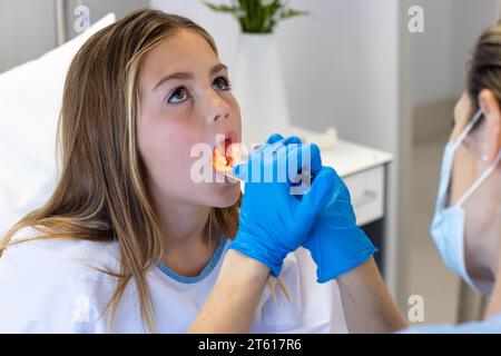 Kaukasische Ärztin in Maske und Handschuhen mittels Fackelprüfung des Rachens einer Patientin im Krankenhaus Stockfoto