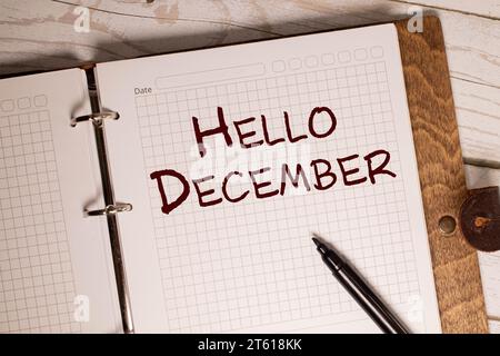 Hallo Dezember Text auf Papier, der aus einem grünen Umschlag mit Neujahrsdekorationen auf einem Holztisch blickt Stockfoto