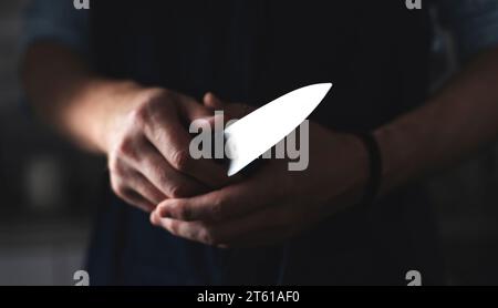 Man's Hands Grip Küchenmesser als Häuptling bereitet sich vor, mit geschärftem Messer vor schwarzem Hintergrund zu kochen Stockfoto