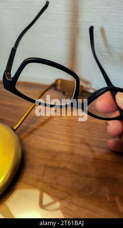 Person, die eine Lesebrille auf dem hölzernen Nachttisch liegen lässt, weil sie müde ist Stockfoto