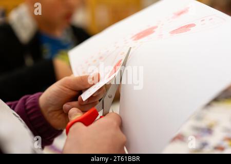 Nahaufnahme von Kinderhänden, die mit einer Schere ein Stück Papier schneiden Stockfoto