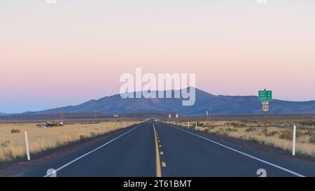 Lange geradlinige Strecke des US Highway 20 im Zentrum von Oregon, die in der Abenddämmerung die High Desert überquert, mit weit entfernten Bergen am Horizont Stockfoto