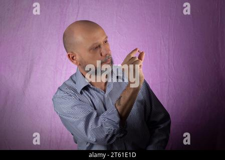 Porträt eines bärtigen, kahlköpfigen Mannes, der eine Pille mit den Fingern vor rosa Hintergrund hält. Stockfoto