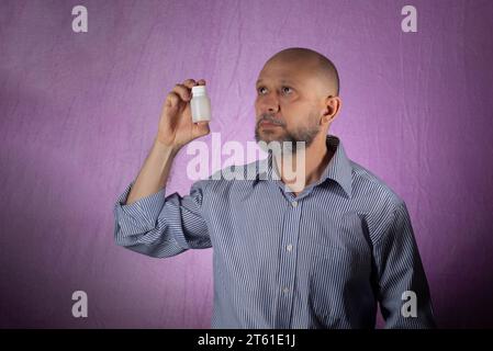 Mann, der weiße Farbverpackungen von Medikamenten vor rosa Hintergrund hält. Stockfoto