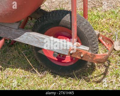 Der vordere Teil und das Rad einer rot verrosteten Schubkarre in einem Garten im Hinterhof Stockfoto