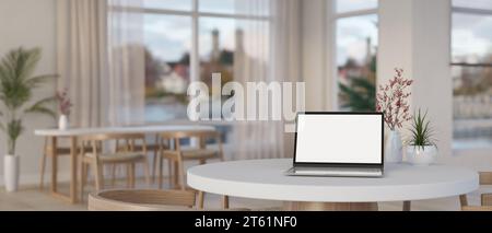 Ein Laptop mit weißem Bildschirm auf einem weißen runden Tisch in einem wunderschönen skandinavischen Café mit erstaunlichen großen Fenstern. Konzept für den Innenbereich. 3D-Rendering Stockfoto