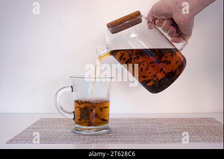 Heißes Wasser, das aus der Teekanne in eine Glasschale mit schwarzen oder roten Teeblättern fließt. Stockfoto