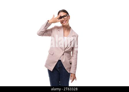 Eine junge positive Brünette mit ihren Haaren in einem Pferdeschwanz, in einer leichten Jacke gekleidet, lächelt und macht ein Gesicht Stockfoto