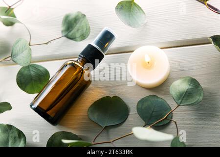 Leere Parfüm-Sprühflasche mit Eukalyptusblättern und Kerze auf weißem Holztisch Stockfoto