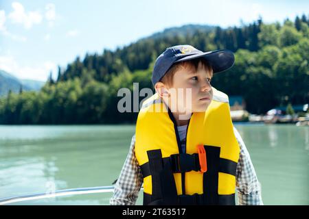 Kleiner Junge, der Sicherheitsweste trägt, fühlt sich krank, wenn er auf dem wunderschönen türkisfarbenen See mit dem Paddelboot segelt. Berge im Hintergrund Stockfoto