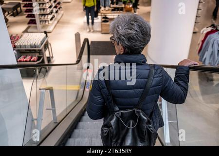 Eine reife Kundin, die mit einer Rolltreppe ins Erdgeschoss in Truro in Cornwall in Großbritannien fährt. Stockfoto