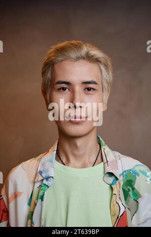 Vertikales Nahporträt eines jungen asiatischen Mannes mit gebleichtem Haar, der im Studio in die Kamera schaut Stockfoto