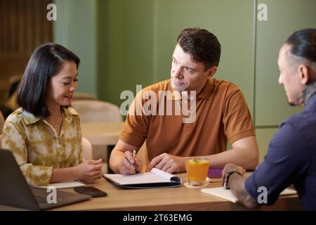 Unterschiedliche Gruppe von Geschäftsleuten, die beim Treffen im Restaurant an Vertragsbedingungen arbeiten Stockfoto
