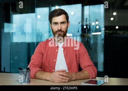 Online-Video-Chat, Remote-Geschäftstreffen, Geschäftsmann im roten Hemd, der ernsthaft nachdenkt und sich in die Kamera konzentriert, Gesprächspartner hört, Webcam-Ansicht, im Büro. Stockfoto