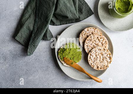 Blick von oben auf Reisbrot auf einem Teller, begleitet von einer lebhaften grünen Spinat-Pesto-Pastasauce in einem Glas, vor grauem Hintergrund in der Nähe der Serviette Stockfoto