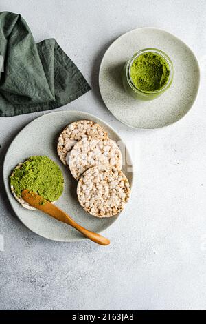 Blick von oben auf Reisbrot auf einem Teller, begleitet von einer lebhaften grünen Spinat-Pesto-Pastasauce in einem Glas, vor grauem Hintergrund in der Nähe der Serviette Stockfoto