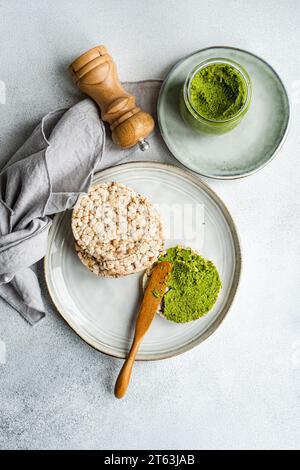 Blick von oben auf Reisbrot auf einem Teller, begleitet von einer lebhaften grünen Spinat-Pesto-Pastasauce in einem Glas, vor grauem Hintergrund in der Nähe von Serviette und s Stockfoto