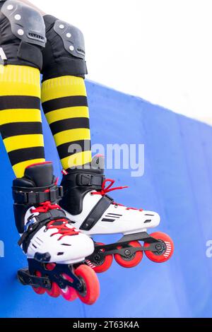 Niedriger Teil der Frau, die gelb gestreifte Socken und Rollschuhschuhe trägt, während sie auf der blauen Wand im Skatepark sitzt Stockfoto