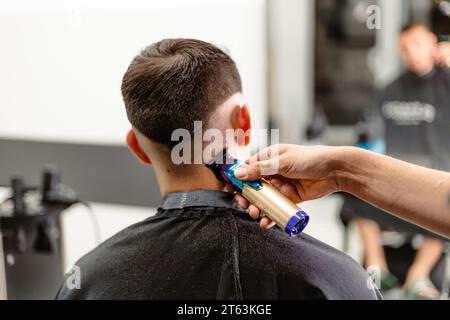 Nahaufnahme der Hand eines Friseurs mit einem mehrfarbigen Haarschneider, um die Haare eines Kunden in einem Salon mit Ausrüstung im Hintergrund zu schneiden. Stockfoto