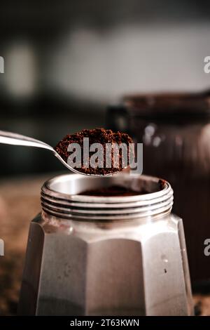 Nahaufnahme von gemahlenem Kaffee aus einem Glas zu einer Espressomaschine aus Edelstahl auf einer gesprenkelten Arbeitsplatte Stockfoto