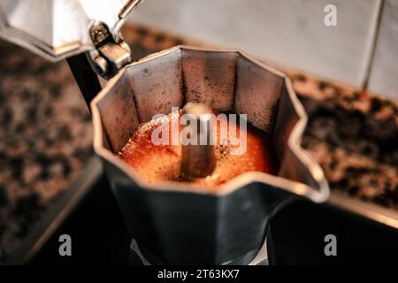 Nahaufnahme von sprudelndem Kaffee in einer Espressomaschine mit offenem Herd, die das reiche Aroma und die Textur des frisch gebrühten italienischen Kaffees in einem gemütlichen setti einfängt Stockfoto