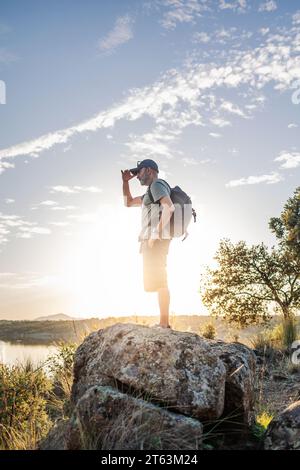 Seitenansicht eines männlichen Reisenden, der auf einem Felsen in Pantano de Layos, Toledo, Spanien steht und in Richtung Horizont blickt, mit einer Hand, die seine Augen abschirmt Stockfoto