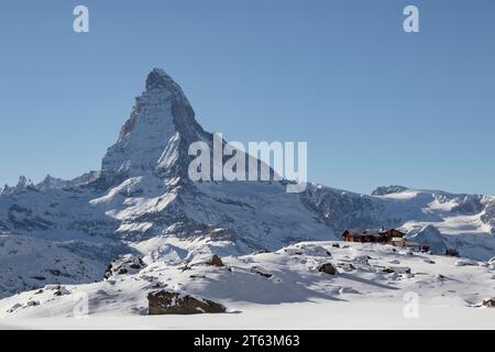 Majestätischer schneebedeckter Berggipfel, der über traditionellen Holzhütten in einer Winterlandschaft thront Stockfoto